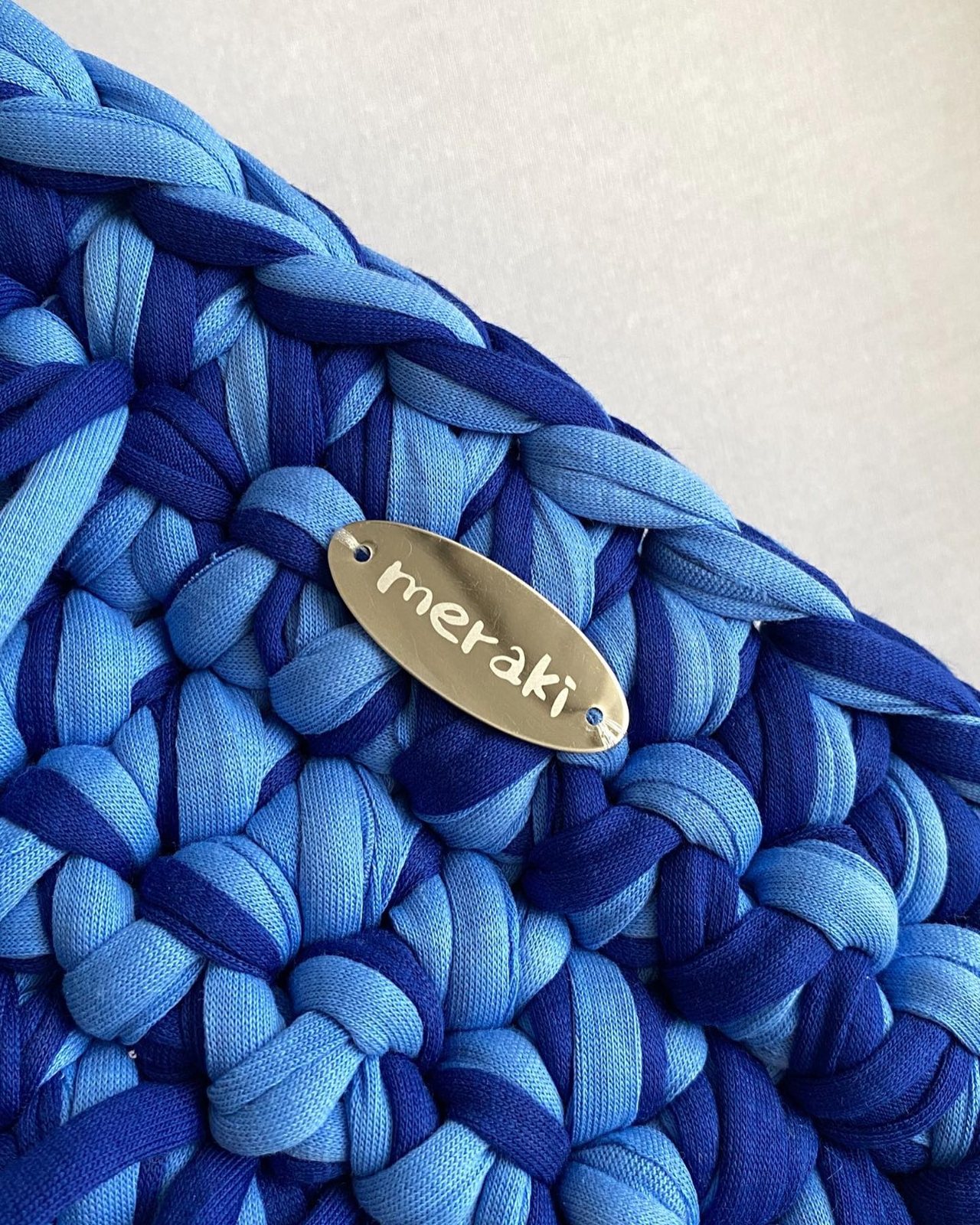 Close-up of blue crochet stitches and the Meraki label