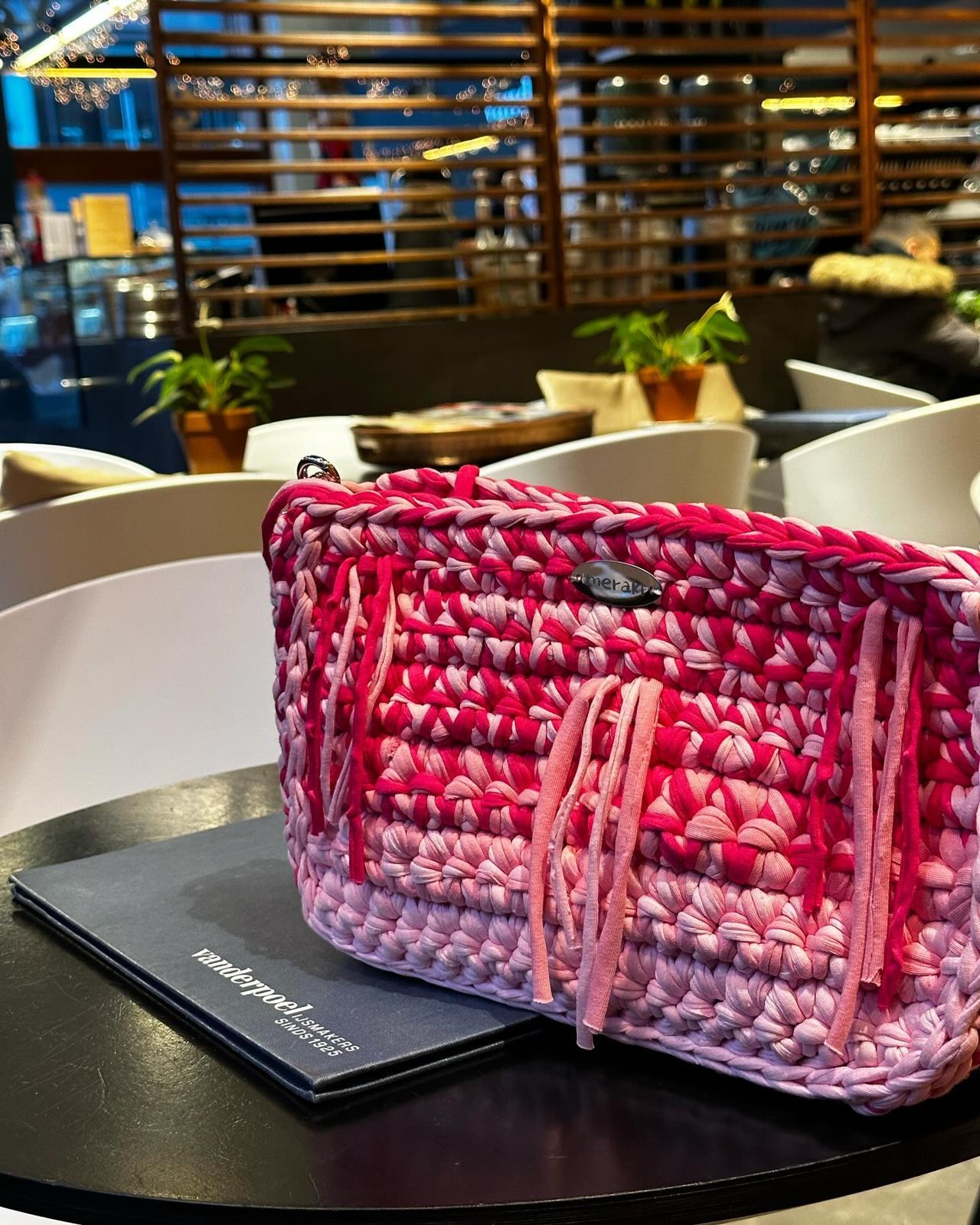 A pink crochet Meraki bag on a café table