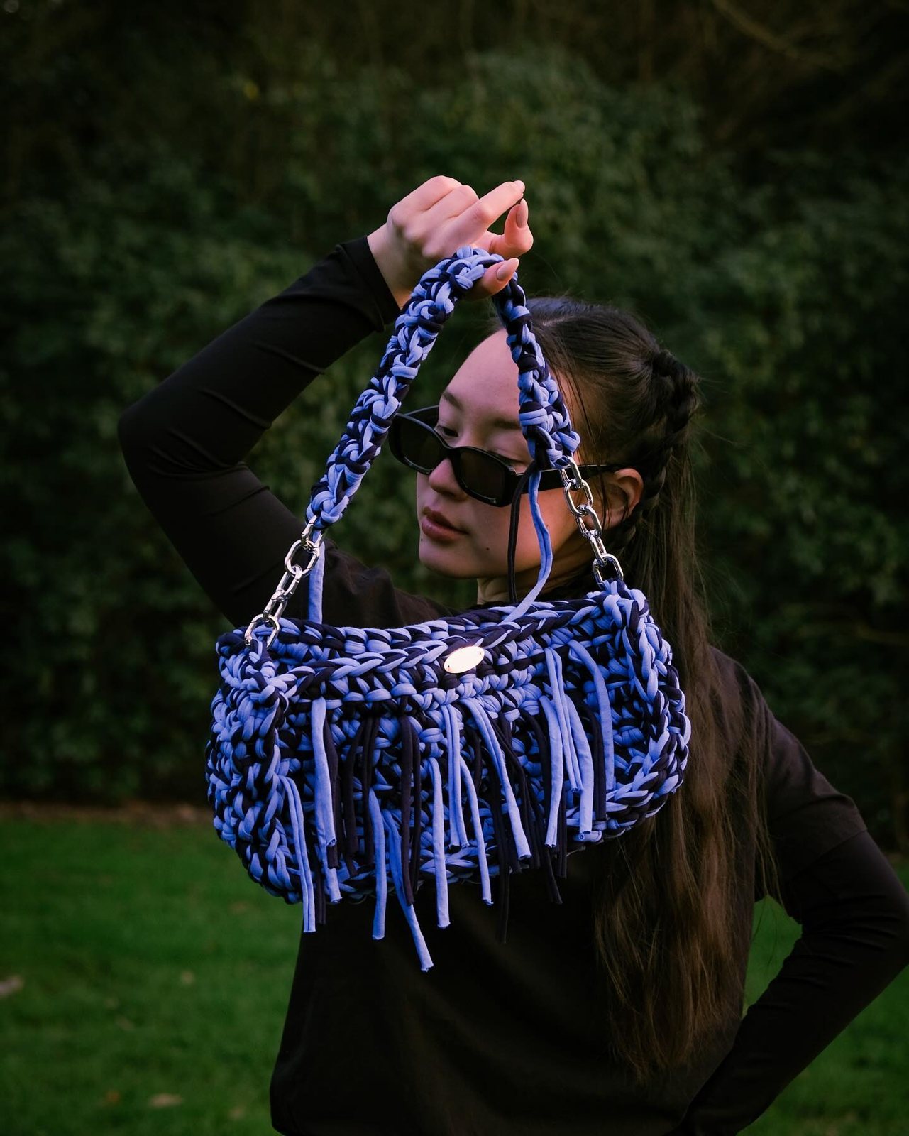 A woman in a park holding a blue crochet Meraki bag