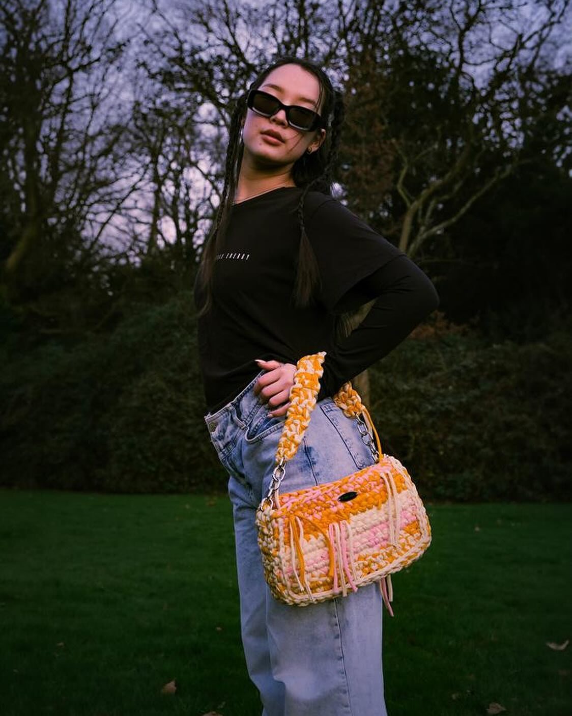 A woman in a park carrying an orange crochet Meraki bag
