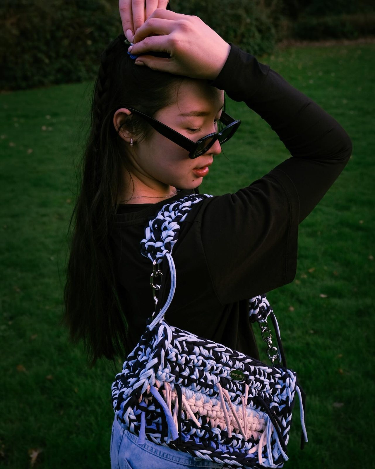 A woman in a park carrying a black-and-white crochet Meraki bag