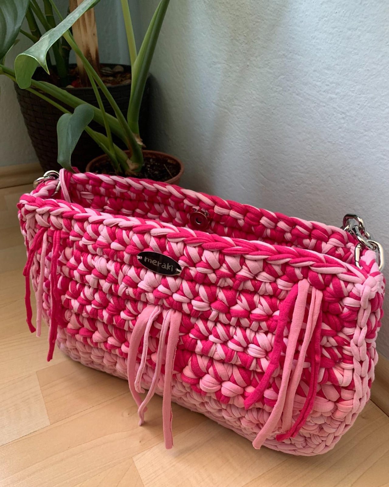 A pink crochet Meraki bag beside house plants