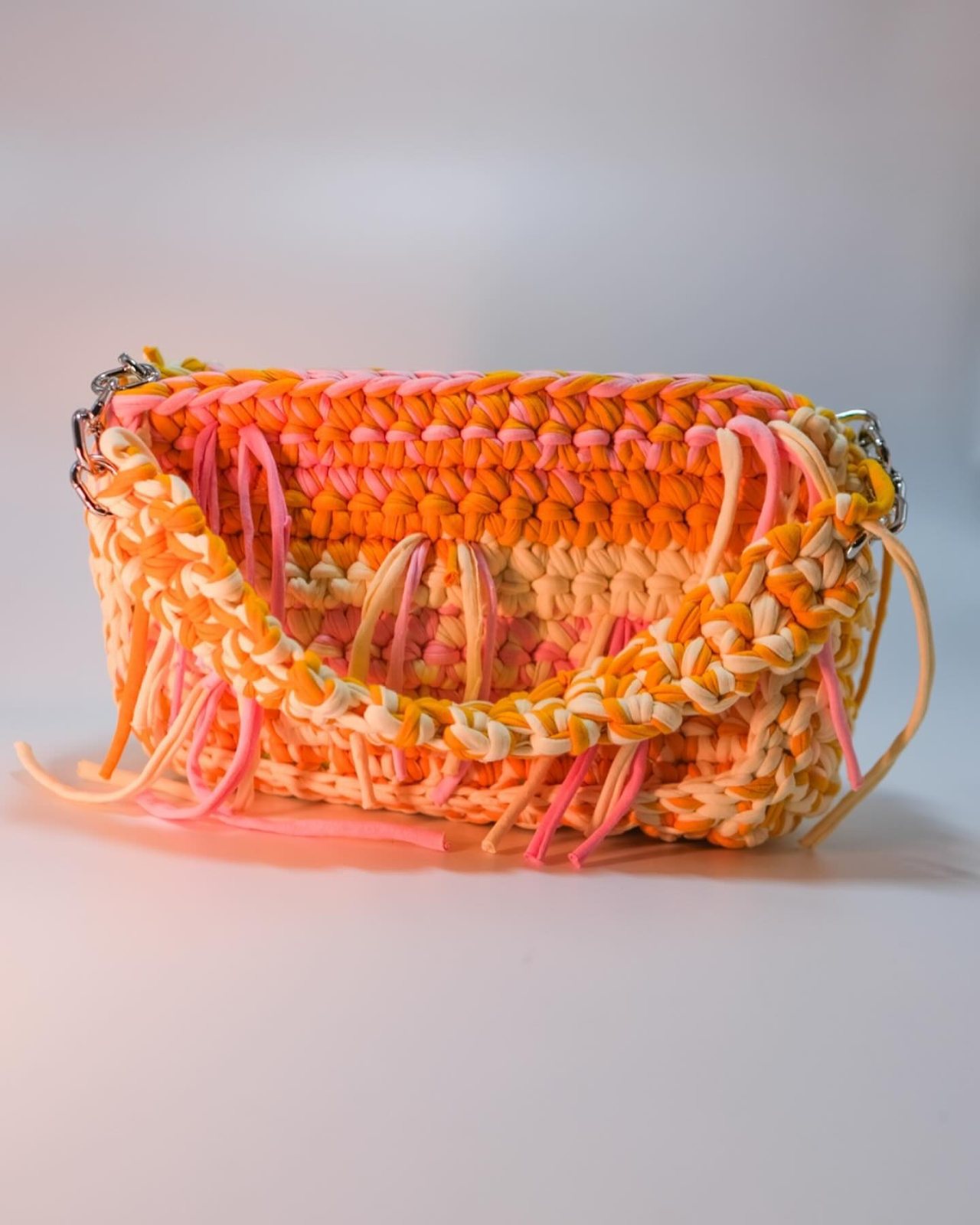 An orange and pink crochet Meraki bag photographed in a studio